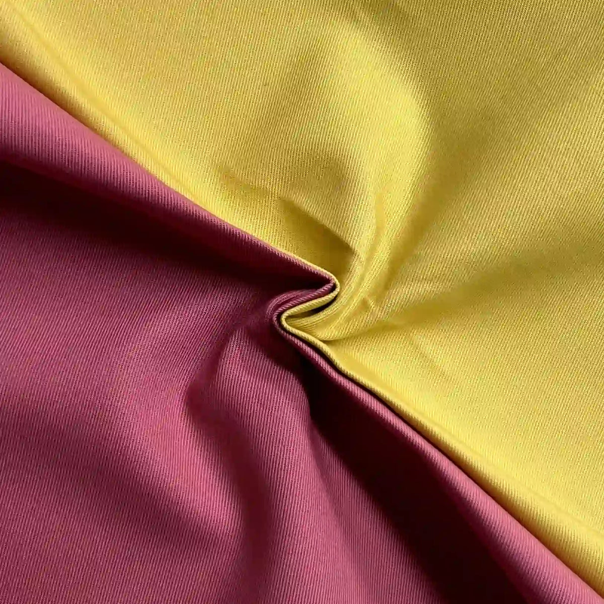 A close-up of Longan Craft Cotton Gabardine Fabric by the yard—one yellow, one maroon—twisted in a swirl to showcase the lightweight twill texture and breathable material, ideal for shirt making.