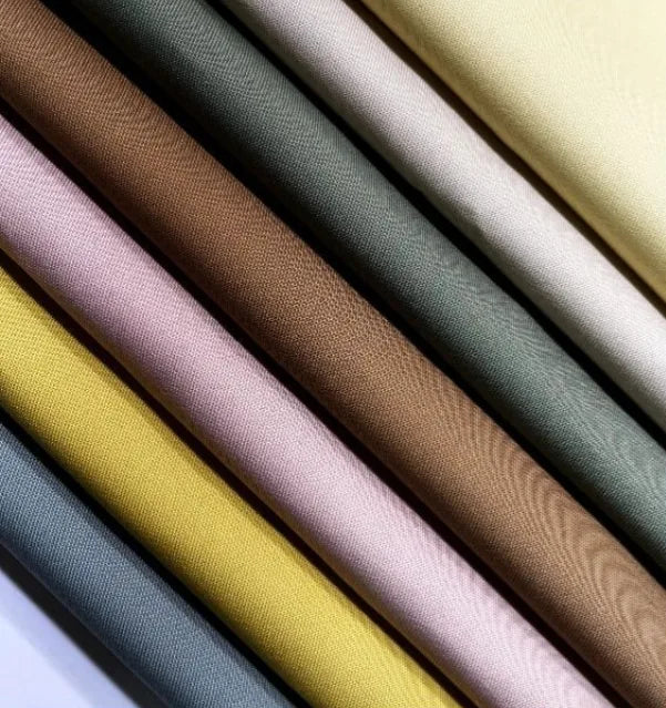 Eight pieces of Longan Craft Cotton Gabardine Fabric By The Yard are arranged in diagonal rows, each a different shade—yellow, pink, brown, green, and blue. This lightweight twill gabardine is smooth, soft, and ideal for shirt making.