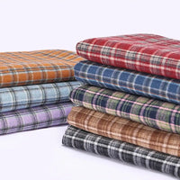 A stack of colorful Cotton Gingham Sueded Flannel Fabric By The Yard from Longan Craft, featuring soft multicolor polyester checked flannel material in shades of red, blue, green, brown, orange, purple, and black—perfect for comfy shirting—neatly arranged against a light background.