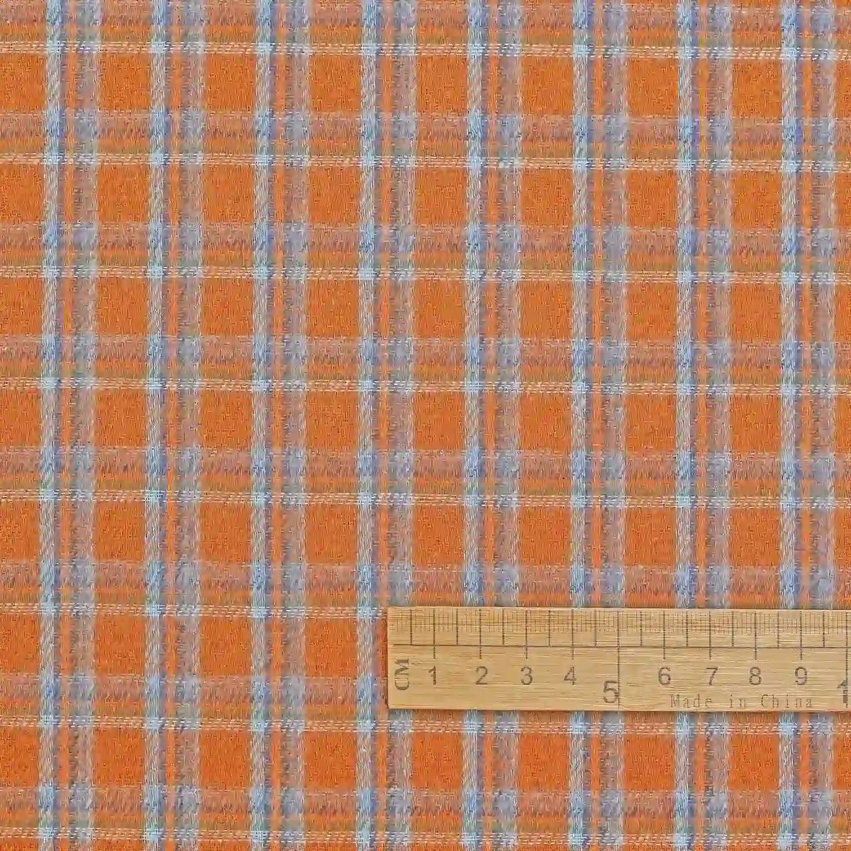 The Cotton Gingham Sueded Flannel Fabric By The Yard from Longan Craft is displayed here featuring a multicolor blue and white check pattern on an orange background. A wooden centimeter-marked ruler at the bottom provides a sense of scale for this comfy polyester flannel material, ideal for shirting and other projects.