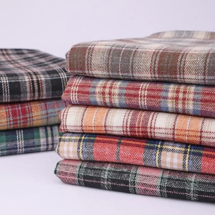 A neatly arranged stack of Longan Craft’s Cotton Jacquard Plaid Flannel Fabric By The Yard showcases a variety of vibrant checkered patterns in red, green, blue, orange, beige, and gray. These cozy autumn flannel pieces are made from one-sided brushed checked cotton jacquard material, perfect for clothing projects, and are set against a plain light background.