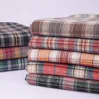 A neatly arranged stack of Longan Craft’s Cotton Jacquard Plaid Flannel Fabric By The Yard showcases a variety of vibrant checkered patterns in red, green, blue, orange, beige, and gray. These cozy autumn flannel pieces are made from one-sided brushed checked cotton jacquard material, perfect for clothing projects, and are set against a plain light background.