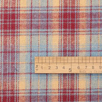 A wooden ruler marked in centimeters lies on red, blue, and yellow plaid fabric from Longan Craft, displaying the scale of the pattern on this soft Cotton Jacquard Plaid Flannel Fabric by the yard—an autumn-ready, one sided brushed checked material ideal for cozy clothing.