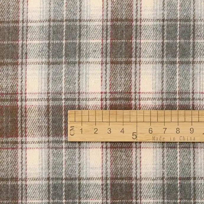 A wooden ruler marked with inches and “Made in China” lies atop the Cotton Jacquard Plaid Flannel Fabric By The Yard from Longan Craft, a soft, beige, brown, and gray checked flannel ideal for cozy autumn clothing projects. This one-sided brushed jacquard fabric is available by the yard.