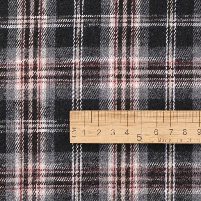 A wooden ruler marked “Made in China” measures approximately 8 centimeters along its edge as it rests on the Longan Craft Cotton Jacquard Plaid Flannel Fabric by the yard—a black, white, and red checked material, one-sided brushed and perfect for cozy autumn clothing projects.