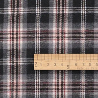 A wooden ruler marked “Made in China” measures approximately 8 centimeters along its edge as it rests on the Longan Craft Cotton Jacquard Plaid Flannel Fabric by the yard—a black, white, and red checked material, one-sided brushed and perfect for cozy autumn clothing projects.