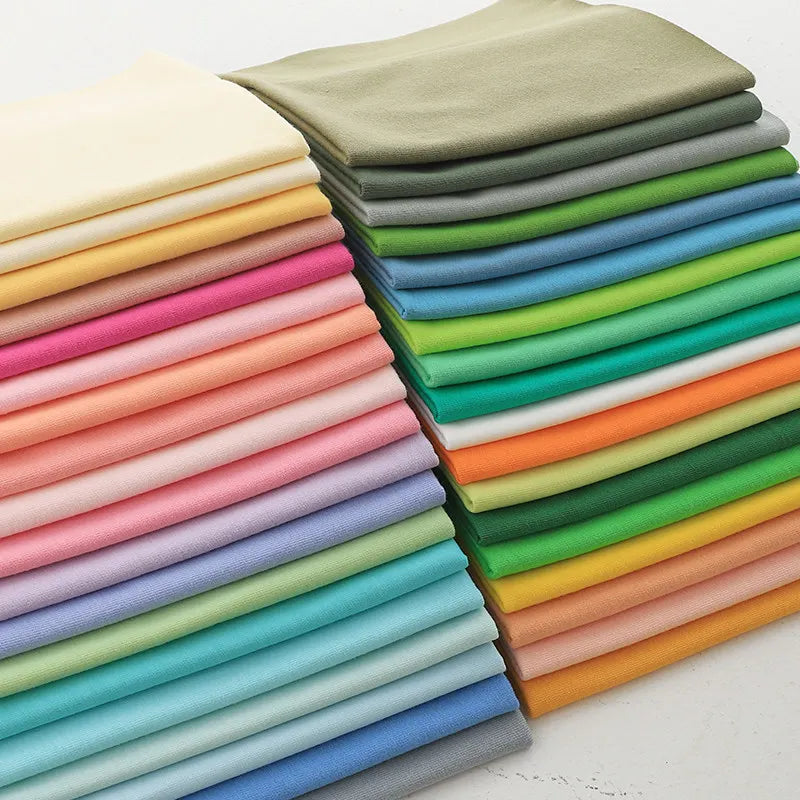 A stack of Longan Craft Cotton Jersey Fabric By The Yard in vibrant shades like yellow, pink, green, blue, orange, and gray is neatly layered on a white surface—soft single jersey material perfect for casual wear.