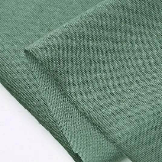 A close-up of Longan Craft’s Cotton Jersey Fabric By The Yard shows its light green, soft, textured cotton surface and fine single jersey weave—ideal for making casual wear.
