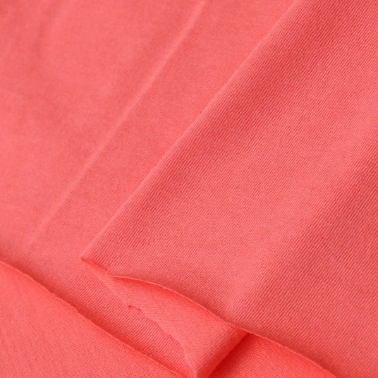 Close-up of Longan Craft Cotton Jersey Fabric by the yard in coral pink, showing its smooth, soft texture and visible weave. This breathable, colorful single jersey material is perfect for making casual wear.