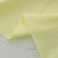 A close-up of Longan Craft’s Cotton Jersey Fabric By The Yard shows its soft, slightly sheer texture in light yellow, gently folded. This colorful single jersey material is ideal for making breathable, casual wear.