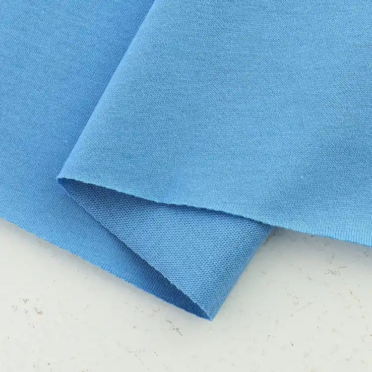 Two pieces of light blue Longan Craft Cotton Jersey Fabric By The Yard are layered on a light surface, showcasing the soft, breathable 100% cotton jersey material, ideal for making colorful casual wear.