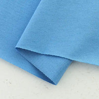 Two pieces of light blue Longan Craft Cotton Jersey Fabric By The Yard are layered on a light surface, showcasing the soft, breathable 100% cotton jersey material, ideal for making colorful casual wear.