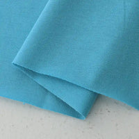 A close-up of two overlapping pieces of Longan Craft's Cotton Jersey Fabric By The Yard in light blue, highlighting the soft, smooth texture and clean edges of this breathable, colorful single jersey fabric for casual wear.