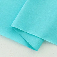 Two pieces of Longan Craft Cotton Jersey Fabric By The Yard in light blue are shown—one flat, one partially folded. This soft, colorful single jersey material has a slightly textured surface, ideal for making casual wear.
