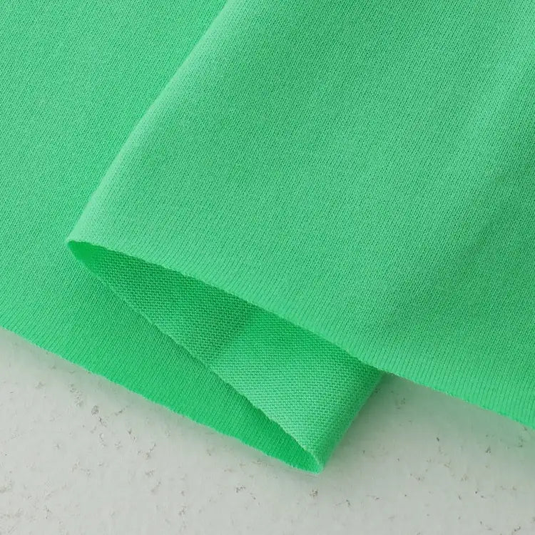 A close-up of the hem of Longan Craft’s Cotton Jersey Fabric By The Yard, a colorful single jersey material with smooth texture and neat stitching, is displayed on a light-colored surface—ideal for making casual wear.