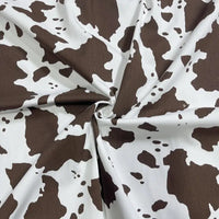 A close-up of Longan Craft's Cow Print Denim Fabric By The Yard shows its brown and white irregular cowhide spots. Made from 100% cotton denim twill, this durable, comfortable material is ideal for DIY handmade clothing projects.