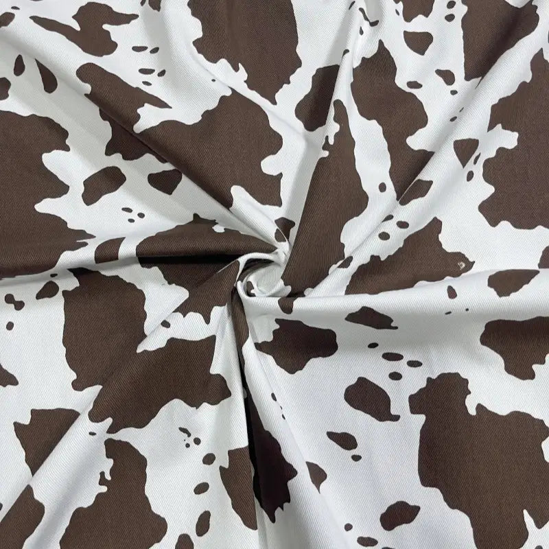A close-up of Longan Craft's Cow Print Denim Fabric By The Yard shows its brown and white irregular cowhide spots. Made from 100% cotton denim twill, this durable, comfortable material is ideal for DIY handmade clothing projects.