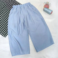 The Wide Leg Capri Pant Sewing Pattern by Longan Craft is shown on a white surface with a black-and-white checkered cloth, blue thread spool, and pincushion—download this free PDF trousers pattern for your next sewing project.
