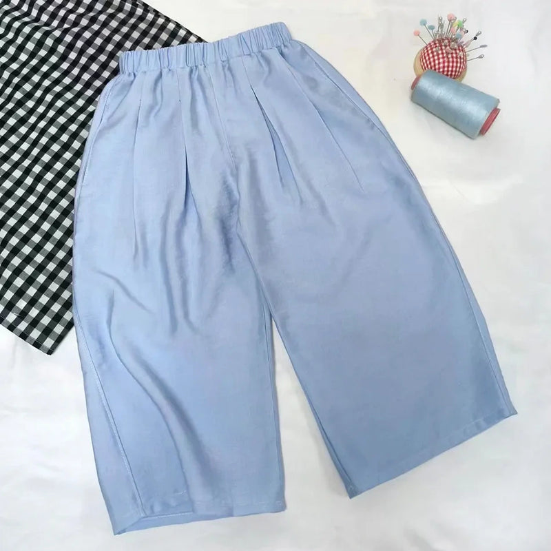 The Wide Leg Capri Pant Sewing Pattern by Longan Craft is shown on a white surface with a black-and-white checkered cloth, blue thread spool, and pincushion—download this free PDF trousers pattern for your next sewing project.