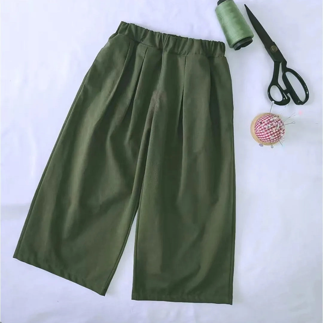 The Wide Leg Capri Pant Sewing Pattern by Longan Craft is displayed beside green thread, black scissors, and a pin cushion on a white background. Download this free PDF trousers pattern to create stylish, high-waisted capris at home.
