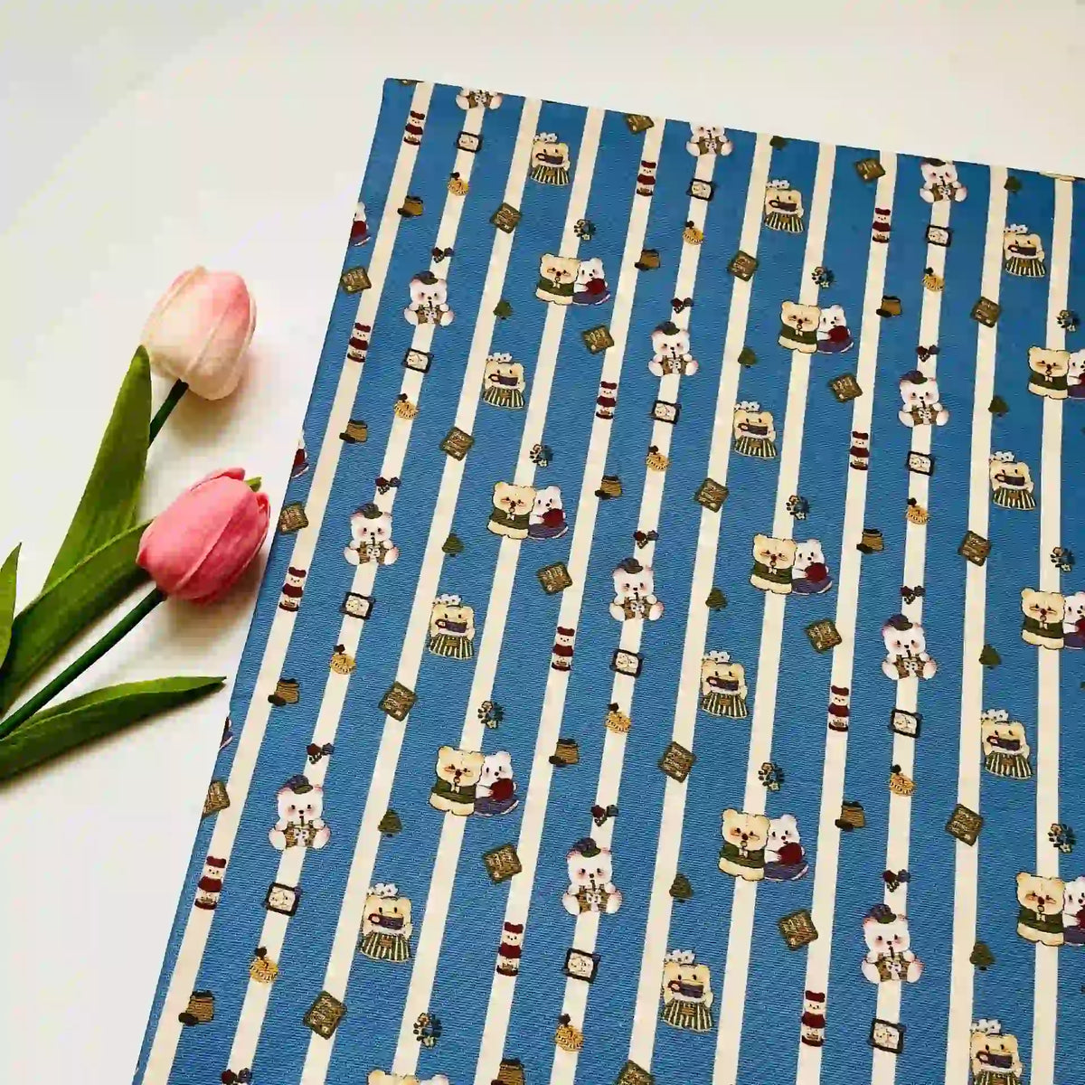 Cute Dog Print Striped Canvas Fabric By The Yard in blue and white with cartoon bears, featuring two pink tulips resting beside it.