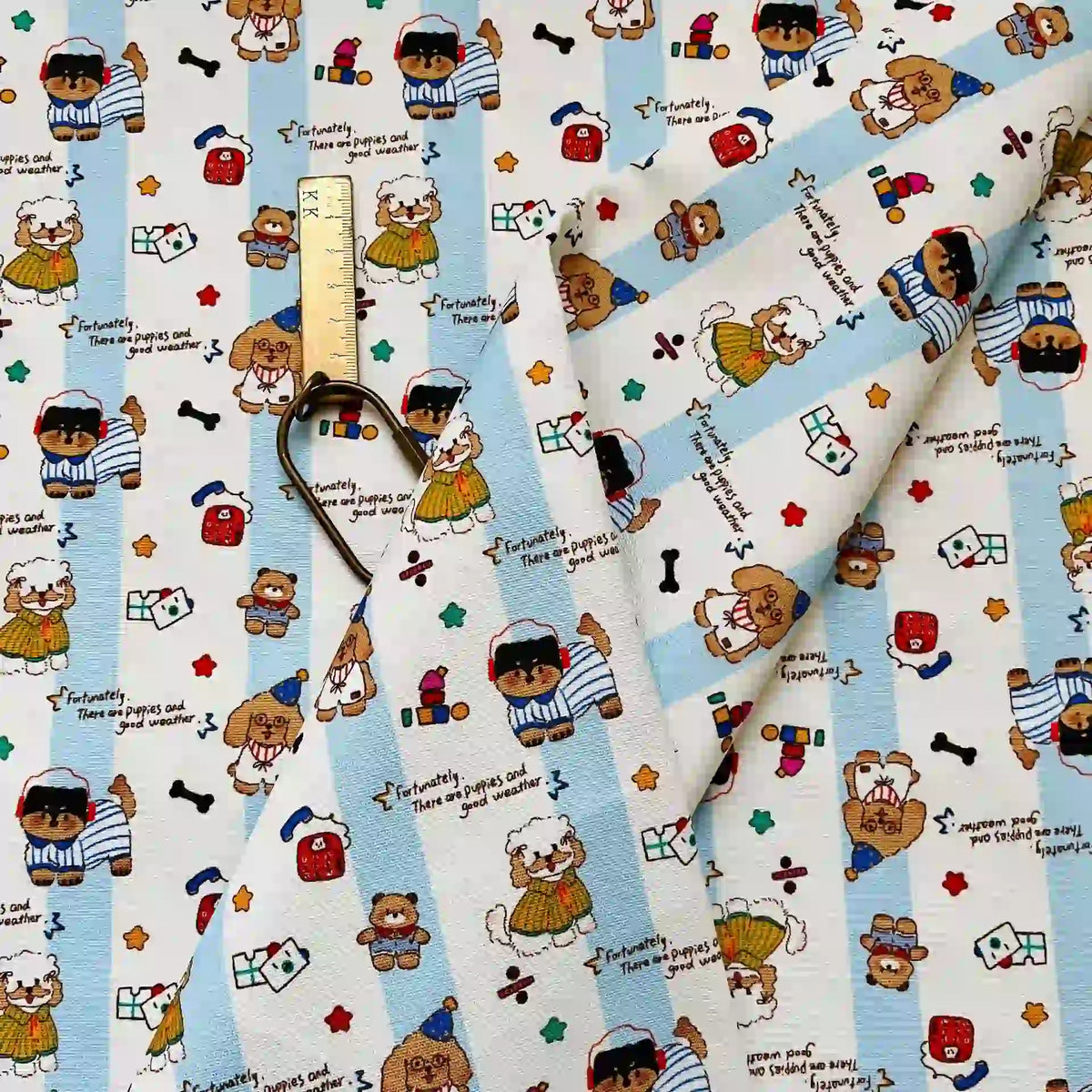 Cute Dog Print Striped Canvas Fabric By The Yard featuring a pattern of cartoon bears, puppies, and hearts on a light blue and white striped background, shown with a metal ruler for scale.