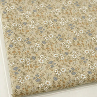 A folded piece of Longan Craft Daisy Print 16 Wale Corduroy Fabric, made from 100% fine wale cotton, displays a quilted beige surface adorned with white daisies, small blue flowers, and brown leaves—a perfect fall corduroy material for DIY projects.