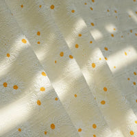 Close-up of Longan Craft’s Daisy Printed Dobby Fabric By The Yard, a cozy cotton material with white daisy patterns and yellow centers, showing off its textured design in natural sunlight and shadow.