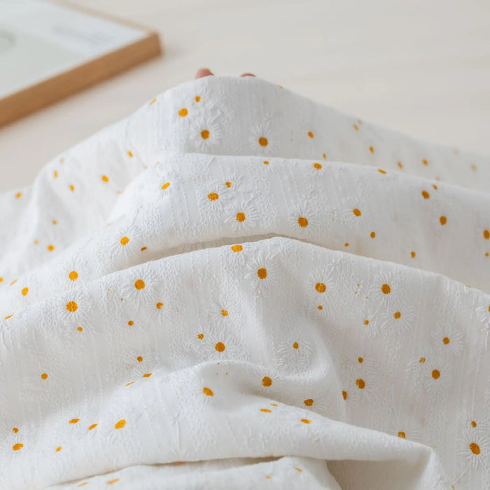 A close-up of Longan Craft's Daisy Printed Dobby Fabric By The Yard shows its cozy, textured cotton surface with small yellow flowers, perfect for clothing and crafted from quality flower-printed cotton dobby material.