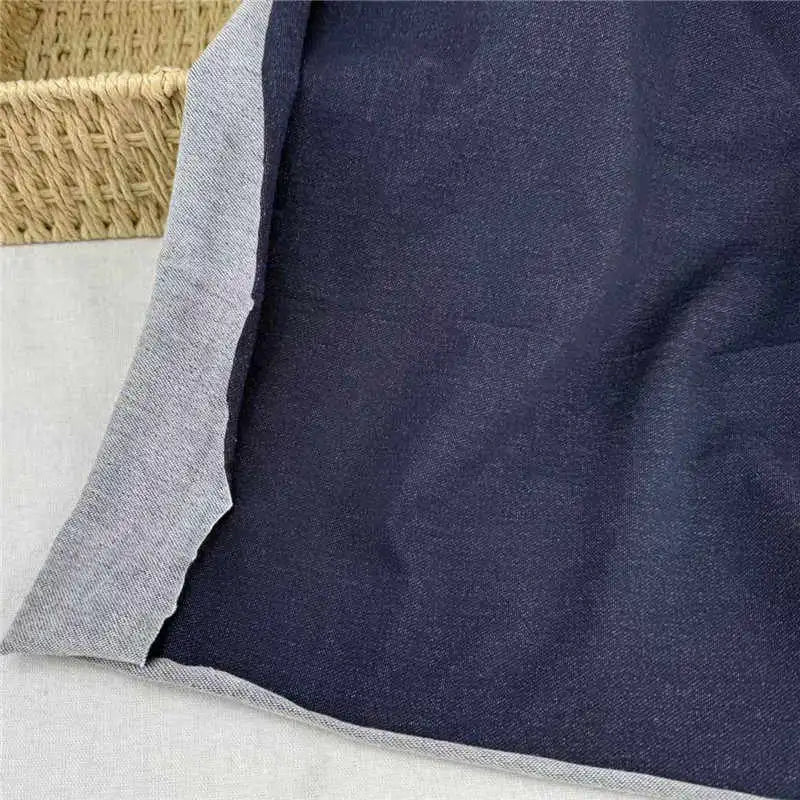 A piece of Longan Craft Denim French Terry Fabric By The Yard is displayed on a light surface, showing both the dark blue top and lighter underside; a woven basket appears in the upper left corner.