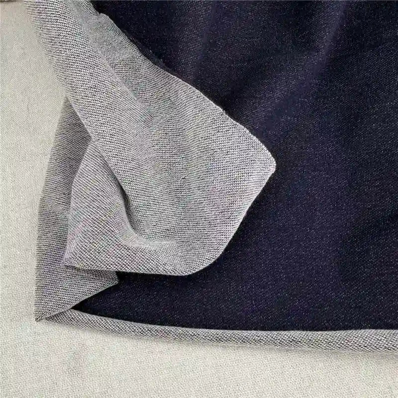 A close-up of Longan Craft’s Denim French Terry Fabric by the Yard, a navy blue 100% cotton knit with a light gray inner lining, partially folded to show both sides. This soft solid-color material is perfect for stylish, comfortable pants.