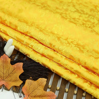 Longan Craft's Dragon Pattern Brocade Fabric By The Yard – a multicolor Chinoiserie vintage cloth with intricate patterns, shown folded on bamboo, accented by two autumn leaves and black tassels.