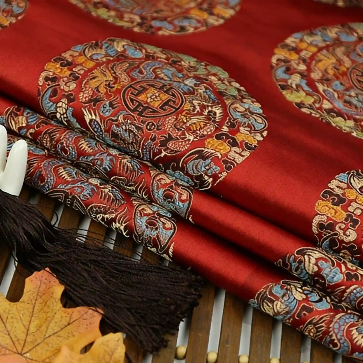 Longan Craft's Dragon Pattern Brocade Fabric by the Yard features multicolor chinoiserie dragon and Chinese motifs on premium vintage brocade, artfully displayed with a brown tassel and autumn leaf. Perfect for crafts and décor.