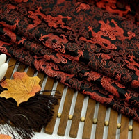 Longan Craft's Dragon Pattern Brocade Fabric By The Yard, a multicolor chinoiserie brocade cloth, is elegantly folded on a bamboo mat with autumn leaves and a dark brown tassel beside it.