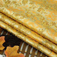 A close-up of folded Dragon Pattern Brocade Fabric By The Yard by Longan Craft, featuring a multicolor chinoiserie floral design, displayed on wood with autumn leaves—ideal vintage brocade cloth material for crafts and décor.