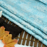 Multicolor Dragon Pattern Brocade Fabric by Longan Craft, featuring vintage Chinoiserie motifs, is beautifully displayed on a wooden surface with brown tassels and autumn maple leaves beside it. Available by the yard.