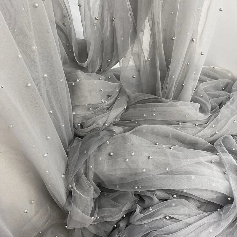The Elegant Pearl Embellished Tulle Fabric by Longan Craft features sheer gray tulle with evenly spaced pearl-like beads—lightweight and perfect for bridal gowns, veils, or other wedding projects. Sold by the yard.