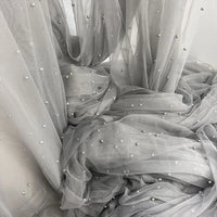 The Elegant Pearl Embellished Tulle Fabric by Longan Craft features sheer gray tulle with evenly spaced pearl-like beads—lightweight and perfect for bridal gowns, veils, or other wedding projects. Sold by the yard.