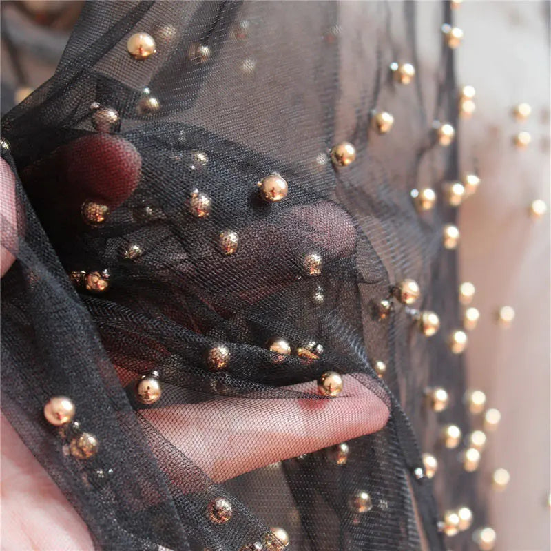 A close-up of a hand holding Longan Craft’s Elegant Pearl Embellished Tulle Fabric—a lightweight, sheer, solid color tulle by the yard with delicate pearl accents. Perfect for weddings or evening gowns.