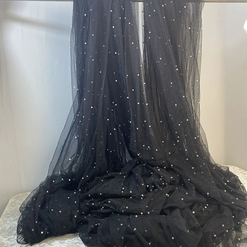 Longan Craft’s Elegant Pearl Embellished Tulle Fabric features solid black, sheer, lightweight material by the yard. Draped over a surface, it cascades into soft folds and subtle transparency for wedding or evening attire.
