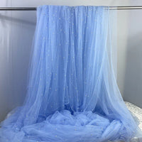 Longan Craft's Elegant Pearl Embellished Tulle Fabric By The Yard features light blue sheer tulle adorned with white pearls, perfect for wedding or evening dresses. Lightweight and elegant, it's ideal for bridal or formal wear projects.