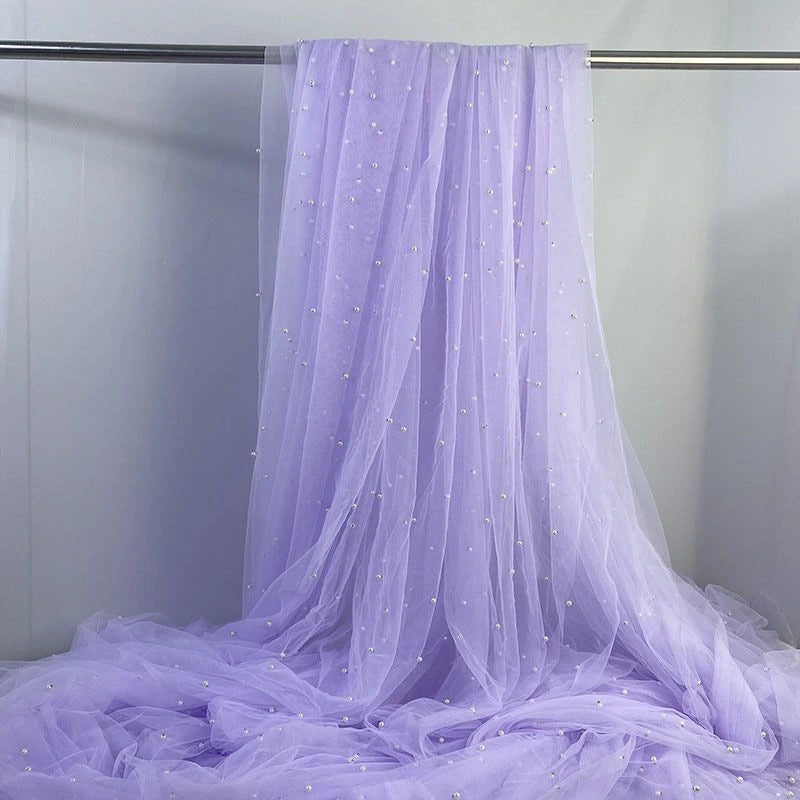 Longan Craft’s Elegant Pearl Embellished Tulle Fabric By The Yard is a sheer, solid lavender tulle adorned with small white pearls, perfect as lightweight wedding décor or drapery.