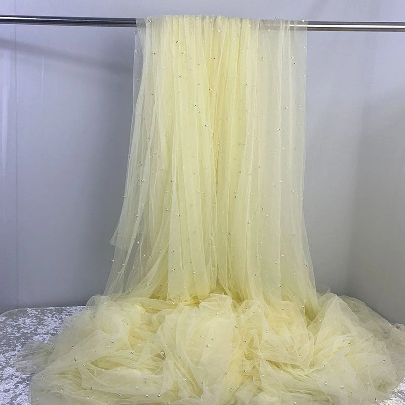 Elegant Pearl Embellished Tulle Fabric by the yard from Longan Craft drapes gracefully with sheer, pale yellow pearl accents—ideal for bridal gowns or evening dresses. This lightweight, solid color tulle is perfect for wedding fashion.
