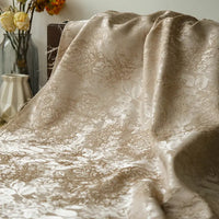 A close-up of Longan Craft's Embossed Peony Brocade Fabric by the Yard, a Chinese-style floral fabric for dresses, draped gracefully with glass and ceramic vases holding dried flowers in the background.