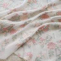 Longan Craft’s Embossed Rose Organza Fabric features gold floral jacquard on sheer, lightweight organza—perfect for camisole tops—elegantly draped over a surface with newspaper text.