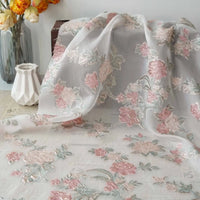 The Longan Craft Embossed Rose Organza Fabric features gold floral jacquard embroidery on sheer, lightweight organza—ideal for camisole tops. It drapes elegantly over any surface with its delicate rose pattern.
