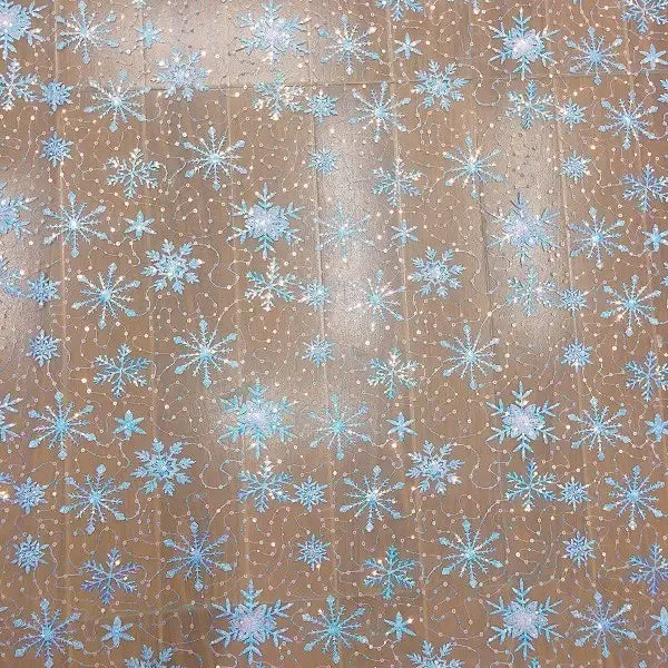 A close-up of Longan Craft’s Embroidered Sequin Tulle Fabric by the yard shows blue snowflake embroidery on a light brown net, ideal for DIY wedding dresses and children's apparel. The detailed sequin outlines evoke embellished tulle designs.