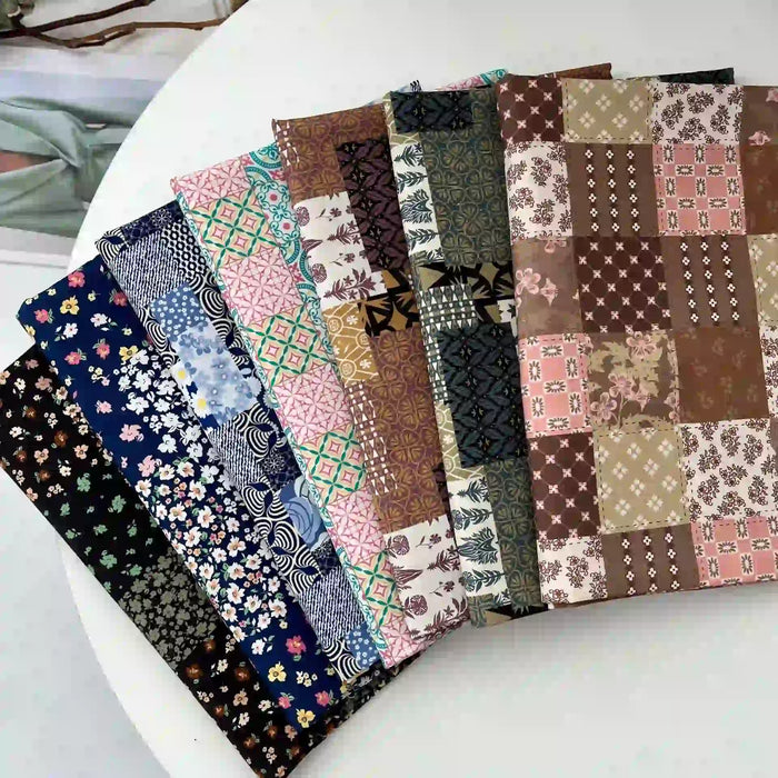 Nine pieces of Longan Craft Ethnic Floral Print Lawn Fabric by the yard, featuring vintage cotton patterns and colorful designs, are neatly arranged in a fan shape on a white round table.