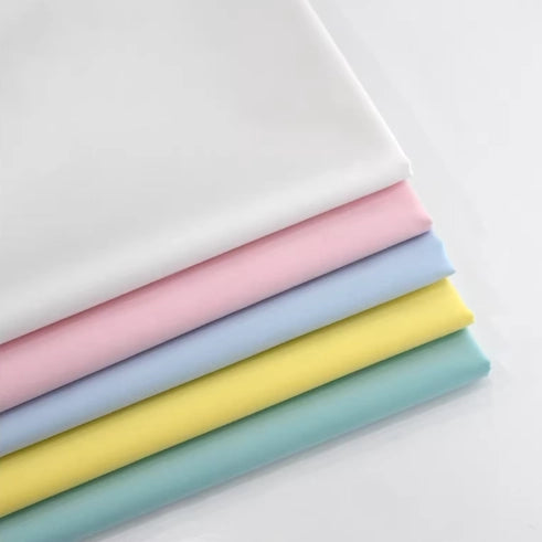 Five neatly folded Longan Craft Fine Cotton Lawn Fabric sheets in white, pink, blue, yellow, and light green—solid pastel colors—are stacked to form an appealing gradient. Perfect lightweight material for casual shirts.