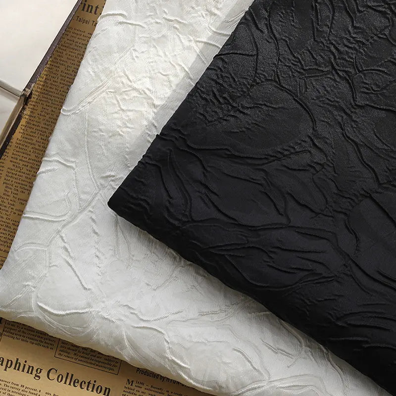Two pieces of Longon Craft Floral Embossed Jacquard Brocade Fabric, one black and one white, with a 3D solid flower pattern, are displayed on vintage newspaper—ideal for party costumes and tailored suits.
